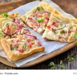 Traditioneller elsässischer Flammkuchen mit Speck und Zwiebeln auf einem Holzbrett serviert