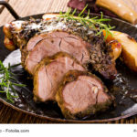 Rustikaler Lammbraten mit feiner Rotwein/Fond-Soße auf einem dunklen Teller angerichtet.