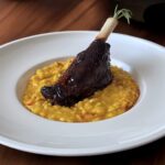 Lammstelze auf Kürbis-Risotto in einem weißen, tiefen Teller angerichtet.