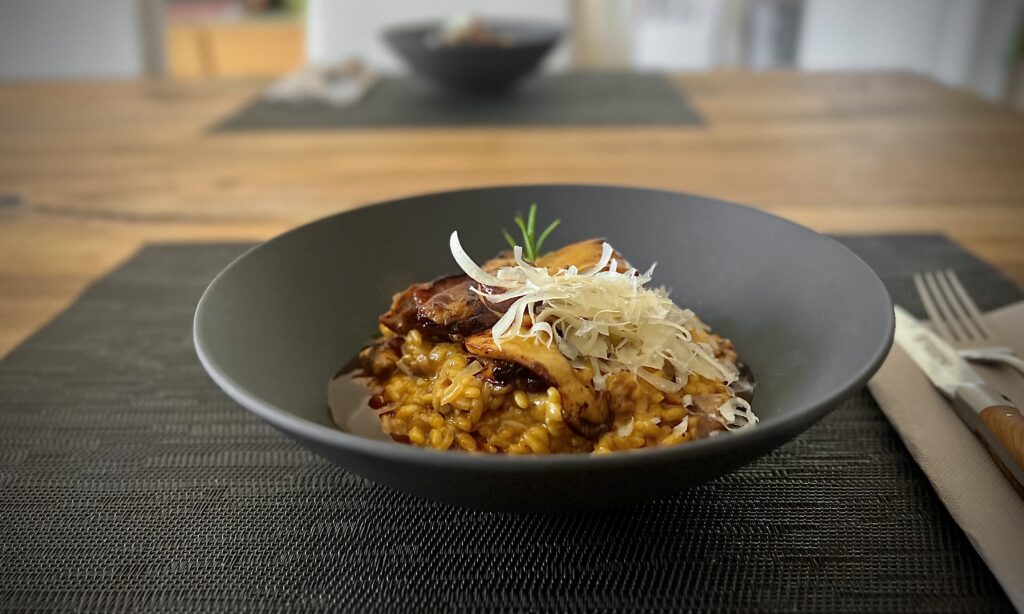 Risotto mit Steinpilzen in einem dunklen Teller serviert und mit gebratenen frischen Steinpilzen dekoriert.