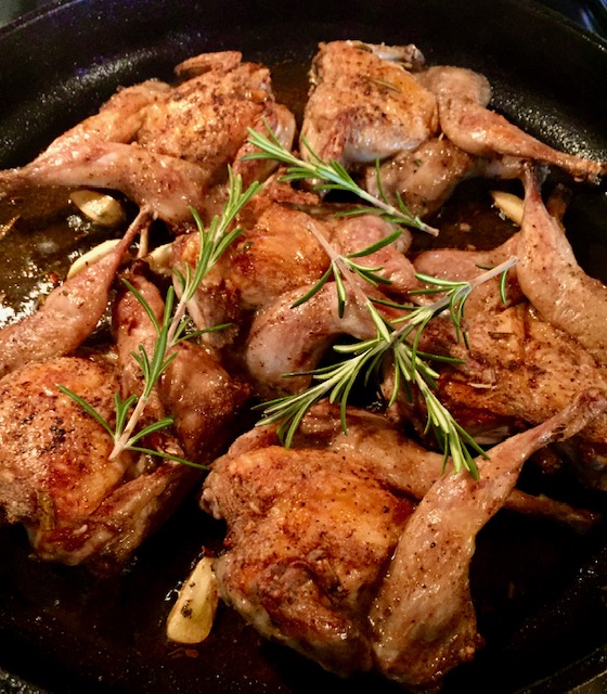 Gebratene Wachteln in der Pfanne mit etwas Rosmarin garniert.