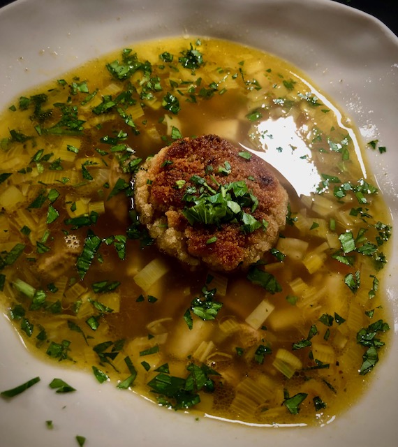 Rinderbrühe mit Kaspressknödel in einem weißen Teller serviert.