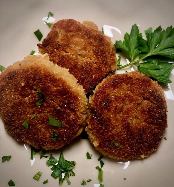 Kaspressknödel auf einem weißen Teller mit frischer Petersilie serviert.