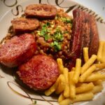 Cotechino mit Linsen, Speck, Salsiccia und Würstchena uf einem Teller serviert.