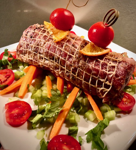 Rollbraten mit mediterranen Zutaten auf einem hellen Teller serviert.