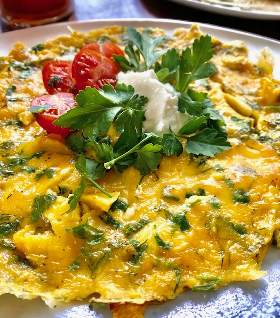 Omelett mit Kräutern, darauf ein paar halbierte Tomaten, Petersiele und etwas Sauerrahm.