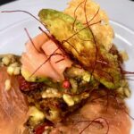 Rösti auf Räucherlachs mit Avocado auf einem weißen Teller serviert.
