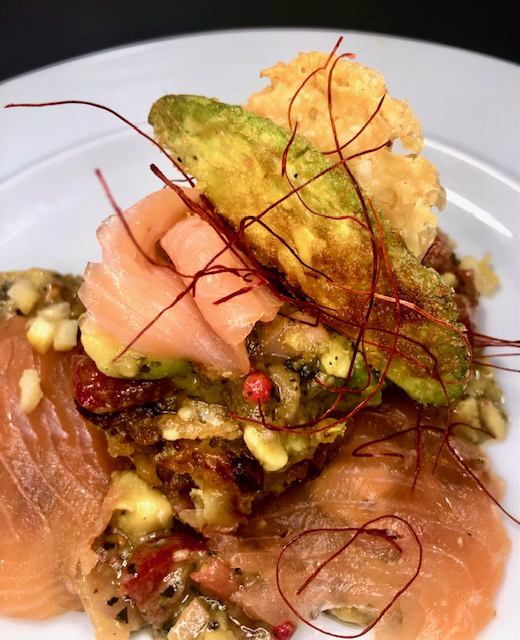 Rösti auf Räucherlachs mit Avocado auf einem weißen Teller serviert.