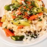 Risotto mit frischem grünem Spargel und Kartoffeln dekorativ auf einem weißen Teller angerichtet.
