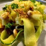 Gurkensalat auf asiatische Art mit gerösteten Sesamsamen und Erdnusskernen auf einem dekorativen Teller angerichtet.