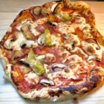 Eine fertige Pizza Regina auf einem Holzbrett.