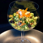 Brokkolisalat mit Äpfeln und Karrotten fein geraspelt in einem Glas angerichtet mit schwarzem Hintergrund.