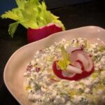Körniger Frischkäse mit Radieschen und Sellerie in einer kleinen Schale angerichtet und mit einem Radieschen und Sellerieblatt garniert.