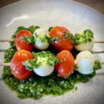 Petersilien-Erdnuss-Pesto auf einem Teller angerichtet mit Mozzarella-Tomaten-Spießchen.
