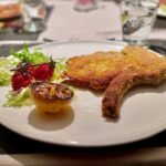Kotelette alla Milanese auf einem hellen Telle mit etwas Salat serviert.
