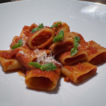 Paccheri - Röhrennudeln mit einfacher Tomatensauce auf einem weißen Teller angerichtet mit Basilikum garniert.