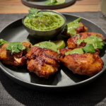 5 Stücke vom peruanischen Grillhuhn mit grüner Sauce auf einen grauen Teller angerichtet und mit Koranderblättern garniert.