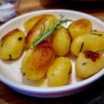 Eine weiße Schüssel mit Kartoffeln und Rosmarinzweigen, serviert als Beilage.