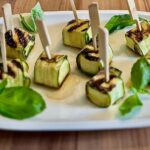 Zucchini-Feta-Päckchen mit Basilikumblättern auf einem weißen Teller angerichtet.