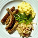 Nürnberger Würstchen mit Sauerkraut und Kartoffelbrei auf einem Teller serviert.