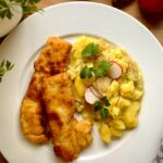 Hähnchenschnitzel mit Kartoffelsalat auf einem weißen Teller serviert.