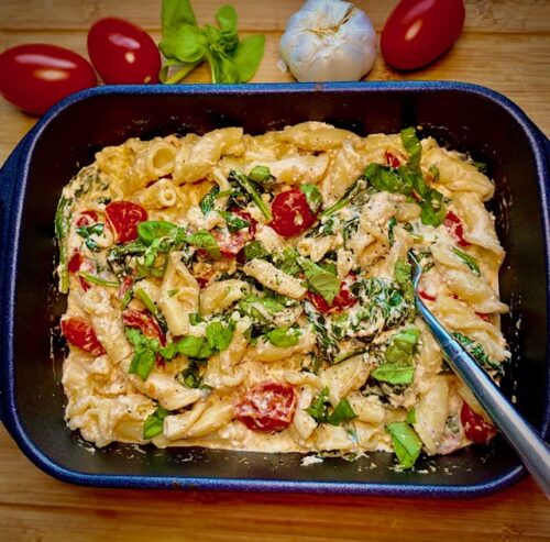 Pasta aus dem Ofen mit Feta, Spinat und Cocktailtomaten in der Auflaufform serviert.