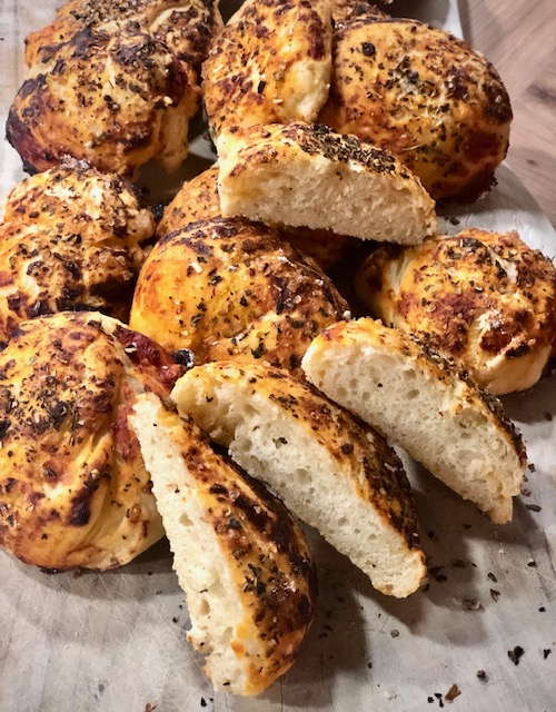 Einige knusprige Pizzabrötchen mit verschiedenen duftenden Kräutern auf einem Brett.
