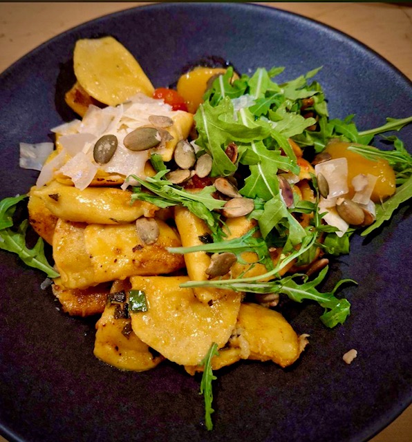 Teigtaschen mit Kürbis-Frischkäse-Füllung auf einem dunklen Teller serviert.