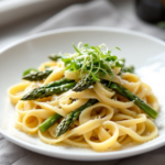 Bandnudeln mit gebratenem grünem Spargel und frischen Sprossen garniert.