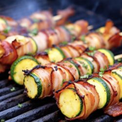 Kartoffel-Zucchini-Spieße mit knusprigen Bacon umwickelt auf einer Grillplatte.