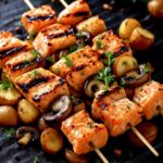 Lachs-Spieße auf einer Grillplatte mit Pilzen und Kartoffeln.