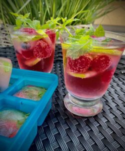 Himbeer-Mojito mit frischen Himbeeren, frischer Minze, Lemonscheiben und fruchtigen Eiswürfeln in einem Glas serviert.