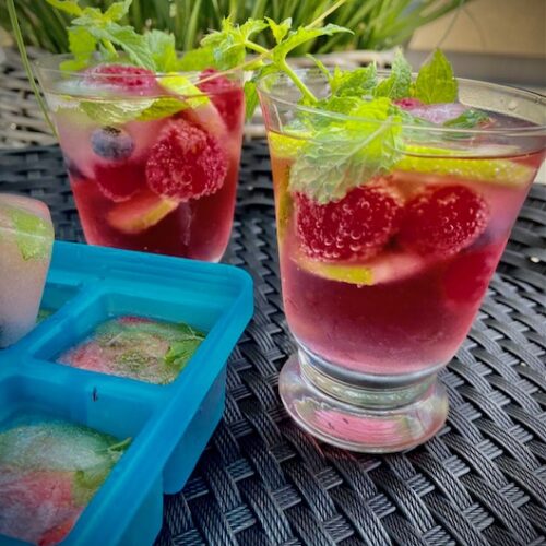 Himbeer-Mojito mit frischen Himbeeren, frischer Minze, Lemonscheiben und fruchtigen Eiswürfeln in einem Glas serviert.