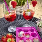 Strawberry-Colada in hohen Gläsern mit frischen Früchten und Eiswürfel mit gefrorenen Früchten, Minze und Basilikum serviert.