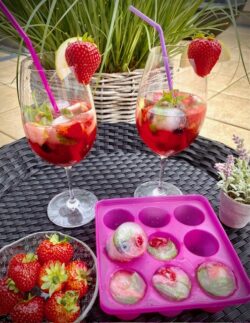 Strawberry-Colada in hohen Gläsern mit frischen Früchten und Eiswürfel mit gefrorenen Früchten, Minze und Basilikum serviert.