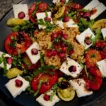 Bulgursalat mit Feta und Granatapfel mit Tomaten auf einem Teller angerichtet.