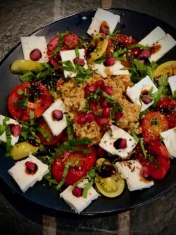 Bulgursalat mit Feta und Granatapfel mit Tomaten auf einem Teller angerichtet.