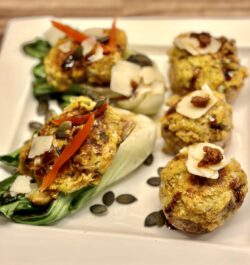 Drei pralle, goldbraune Champignons, gefüllt mit einer würzigen Falafel-Mischung, ruhen auf einem Bett aus knackig gegrilltem Pak Choi. Bestreut mit leuchtend grünen Kürbiskernen und feinem Parmesan, vollendet durch die dunkle Spur einer Balsamico-Creme. Ein Fest für die Sinne.
