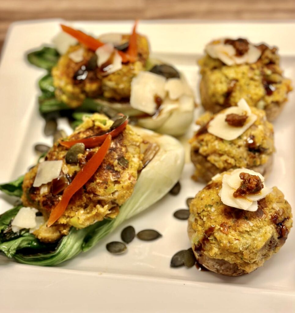 Drei pralle, goldbraune Champignons, gefüllt mit einer würzigen Falafel-Mischung, ruhen auf einem Bett aus knackig gegrilltem Pak Choi. Bestreut mit leuchtend grünen Kürbiskernen und feinem Parmesan, vollendet durch die dunkle Spur einer Balsamico-Creme. Ein Fest für die Sinne.
