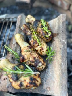 Eine alte Dachziegel auf dem Grill mit saftigen Hähnchenkeulen und frischen Rosmarien.