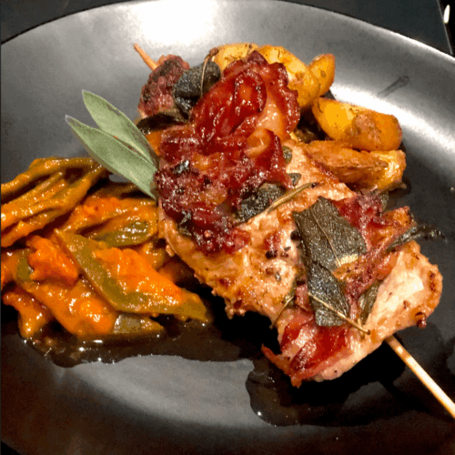 Saltimbocca mit Rosmarinkartoffeln und Bohnengemüse auf einem schwarzen Teller angerichtet.