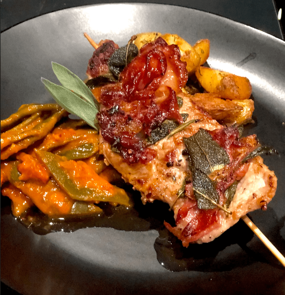 Saltimbocca mit Rosmarinkartoffeln und Bohnengemüse auf einem schwarzen Teller angerichtet.