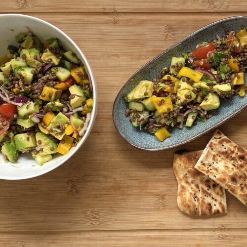 Linsensalat in einer Schüssel und auf einem Teller mit getoastetem Naan-Brot auf einer Holzplatte serviert.