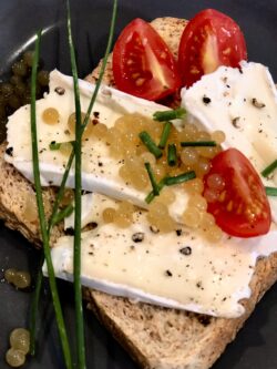Vegetarische-Kaviar-Perlen-aus-Agar-Agar auf einem Toast Brot mit Camembert und Tomate sowie Schnittlauch garniert.