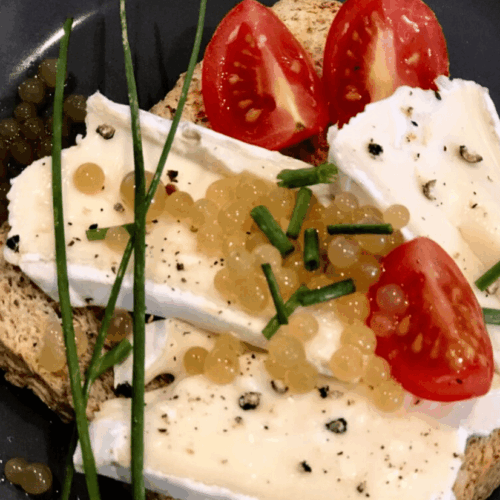 Vegetarische-Kaviar-Perlen-aus-Agar-Agar auf einem Toast Brot mit Camembert und Tomate sowie Schnittlauch garniert.