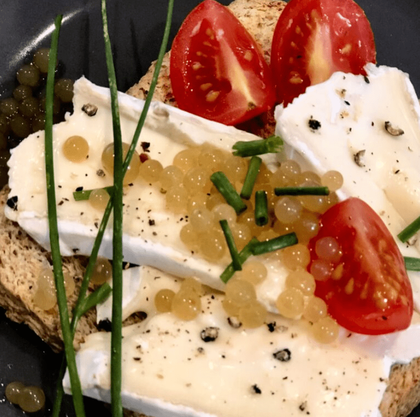 Vegetarische-Kaviar-Perlen-aus-Agar-Agar auf einem Toast Brot mit Camembert und Tomate sowie Schnittlauch garniert.