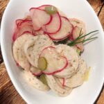 Bayrischer Weißwurst-Salat in einer weißen Schüssel serveriert.