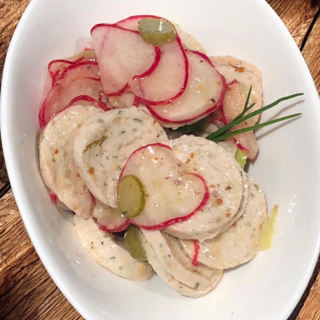 Bayrischer Weißwurst-Salat in einer weißen Schüssel serveriert.