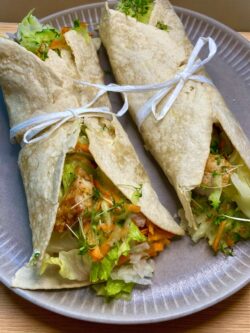 Wrap's mit gebratenen Hähnchenstreifen, Käse und Salat auf einem hellen Teller angerichtet und mit einer Schleife dekoriert.