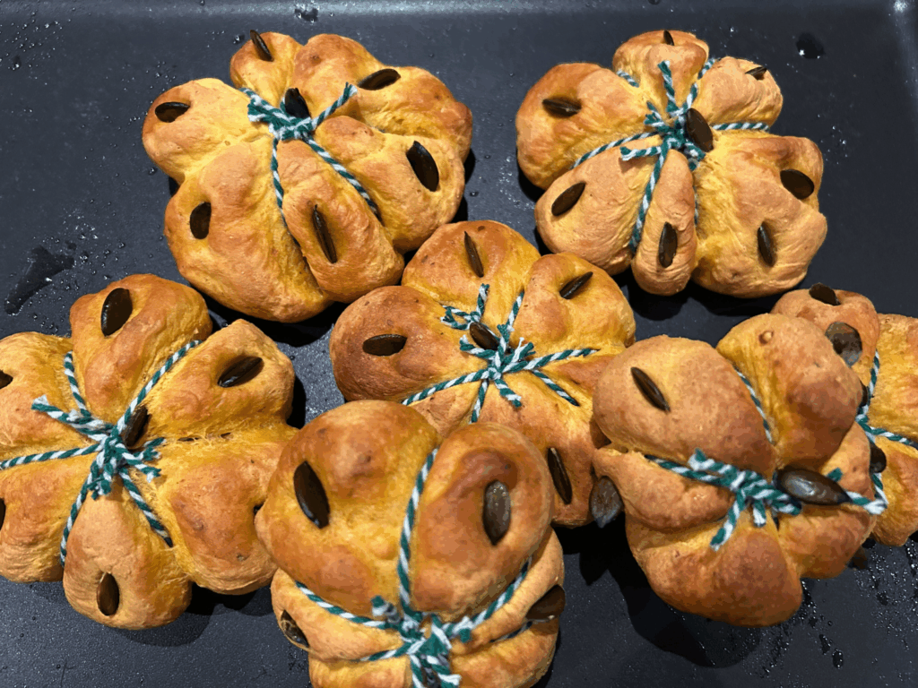 Halloween-Kürbisbrötchen mit grünem Garn auf einer dunklen Schieferplatte.